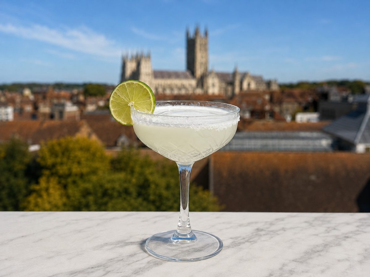 A classic cocktail in a coupe with a lime wheel, Canterbury Cathedral behind