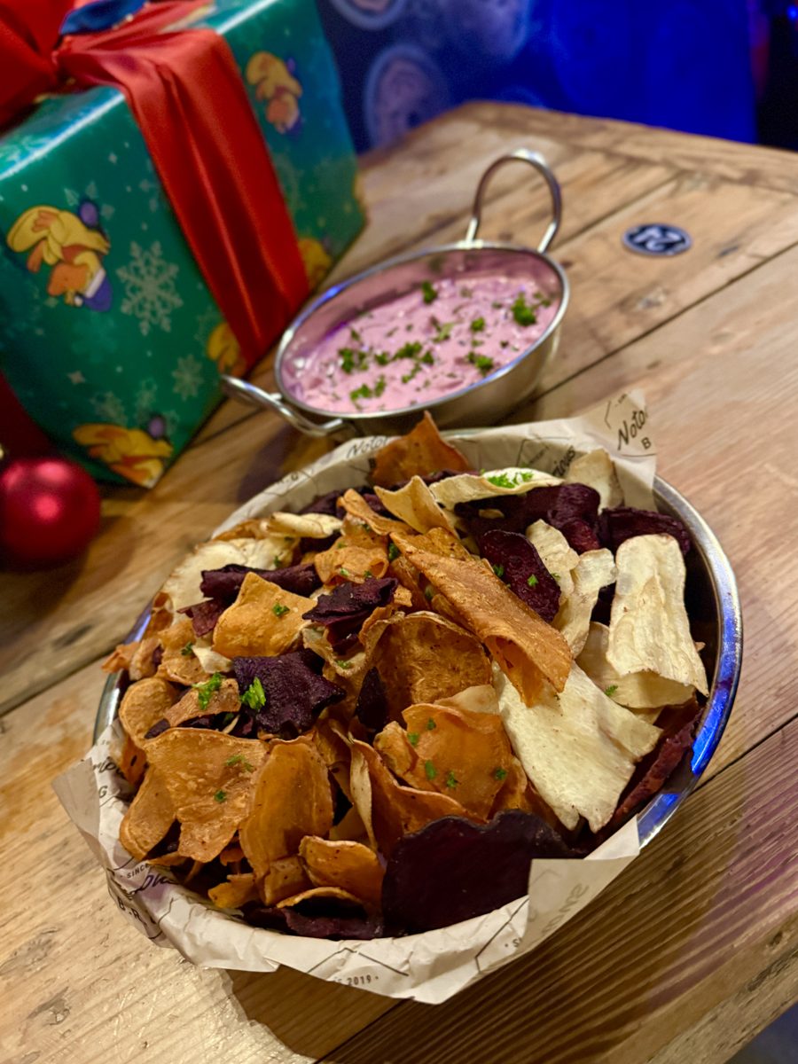 A bowl of vegetable crisps with a pink dip beside a wrapped present